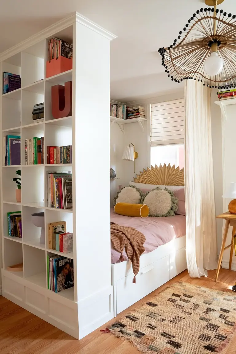 Stunning Kallax Bedroom Transformations You Need to See 2 A tall white cube shelf standing as a divider beside a bed nook with pink bedding, a desk with a lamp, a patterned rug, and a window behind the bed