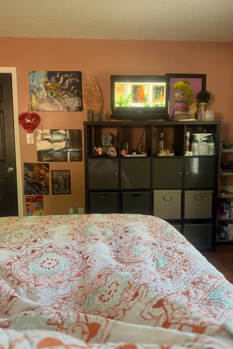 Stunning Kallax Bedroom Transformations You Need to See 3 A bedroom seen from the bed, with a black Kallax cube unit standing opposite the bed, a television on top, posters on the wall, and patterned bedding in the foreground