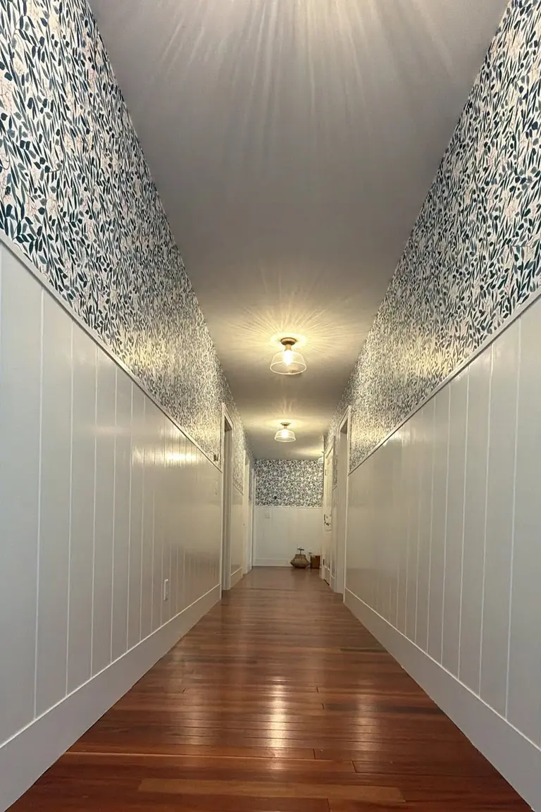 Long hallway with white beadboard wainscoting and leaf patterned wallpaper above