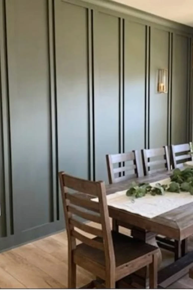 25 Stunning Accent Wall Ideas for Every Room and Style 4 A dining room with a full-height dark green board-and-batten accent wall running behind a long wooden dining table set parallel to the wall, with wooden chairs, a bench, a chandelier, and a window