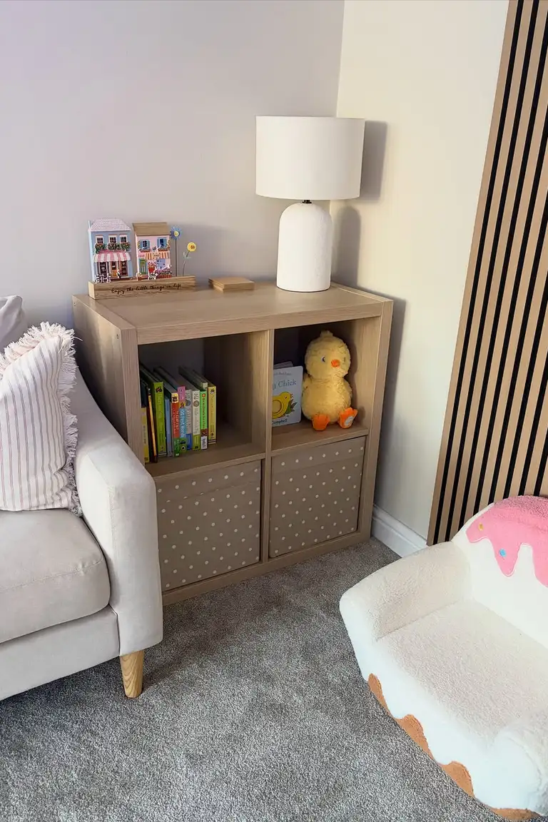 Stunning Kallax Bedroom Transformations You Need to See 7 A light-wood 2x2 Kallax cube unit with children's books, a plush chick toy and a lamp on top, beside a sofa and a small cake-shaped child armchair on grey carpet