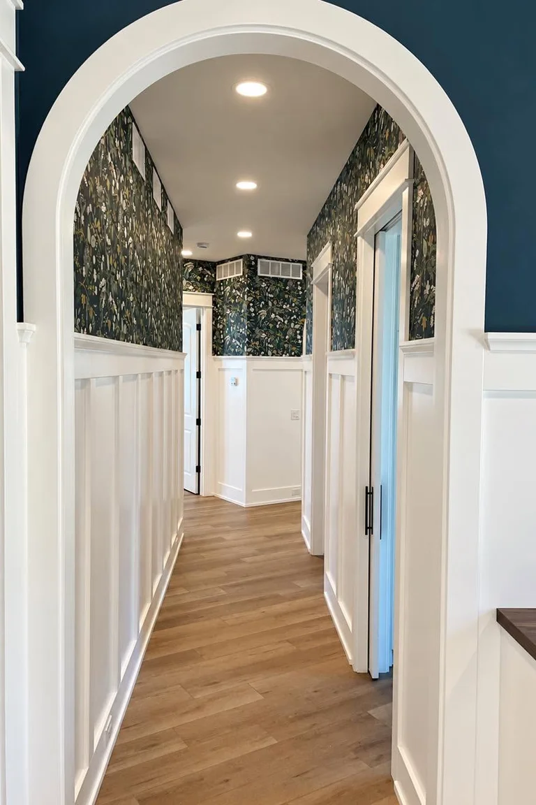 Narrow hallway with white board and batten wainscoting seen through an arched opening