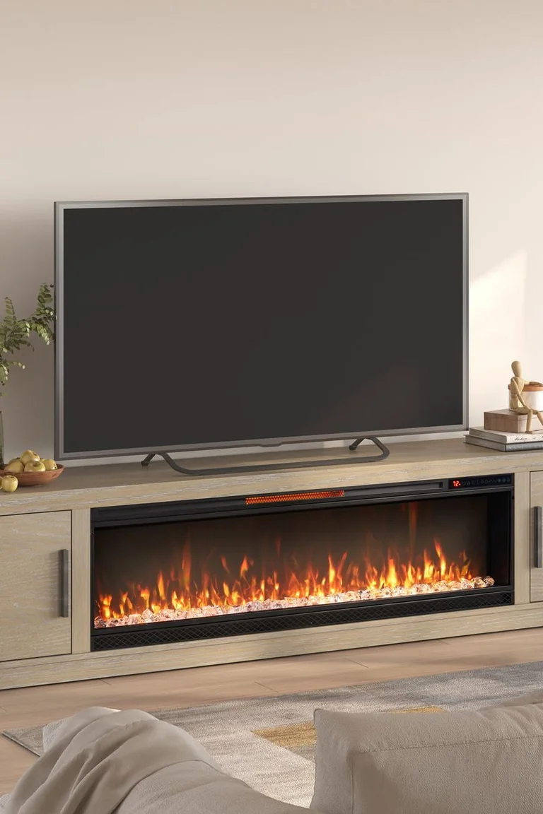 A freestanding light wood media console with closed cabinets and an integrated electric fireplace, with a large television standing on top, a sofa and rug in front.