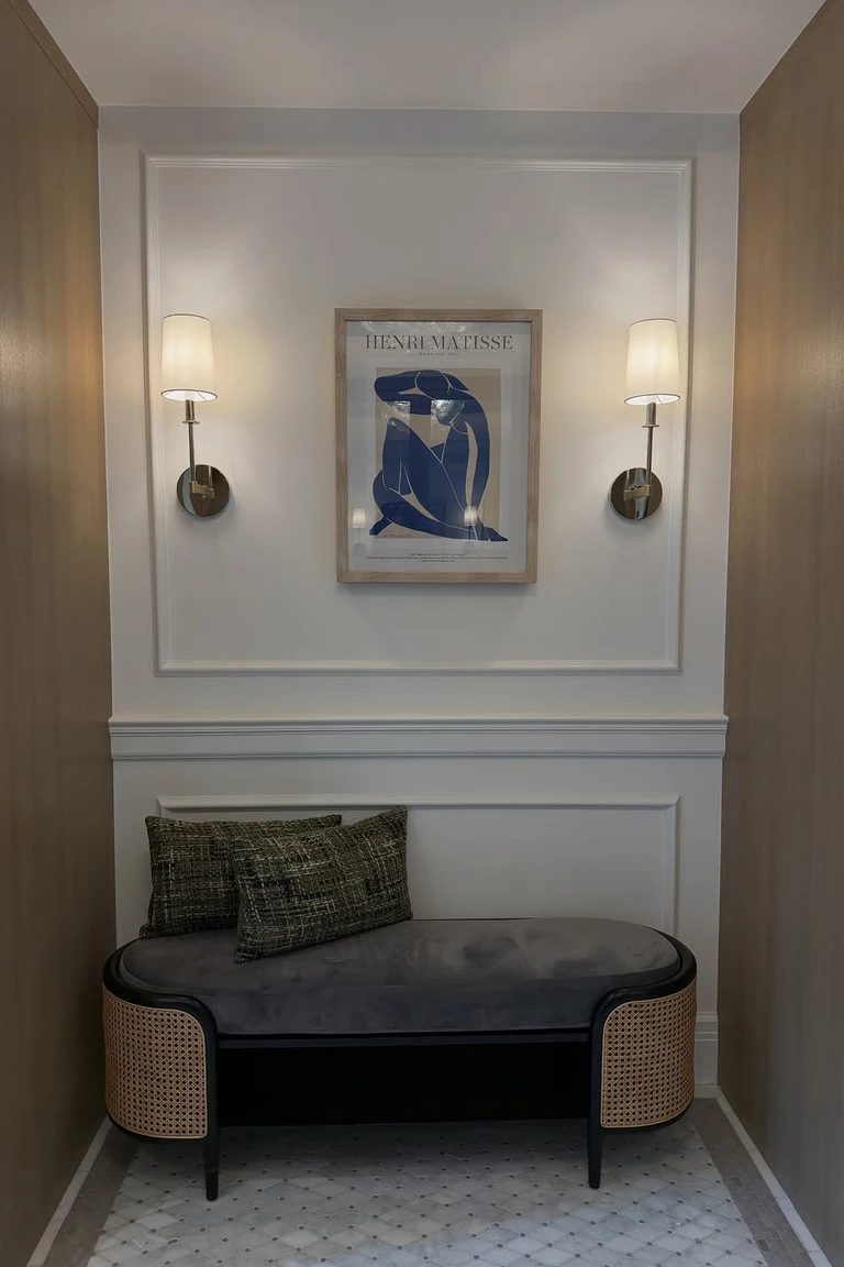 Small entry nook with white picture frame molding, wall sconces and a bench