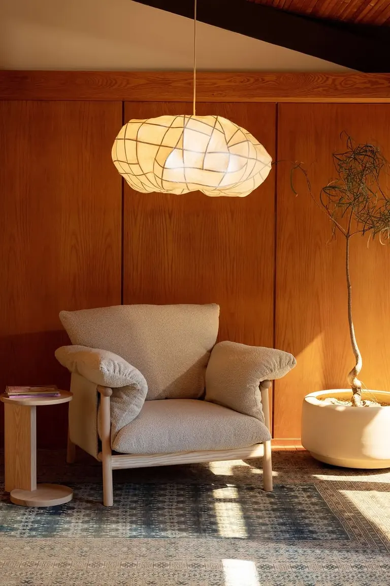 Tall potted tree standing beside a boucle armchair in a corner, adding height to the setup