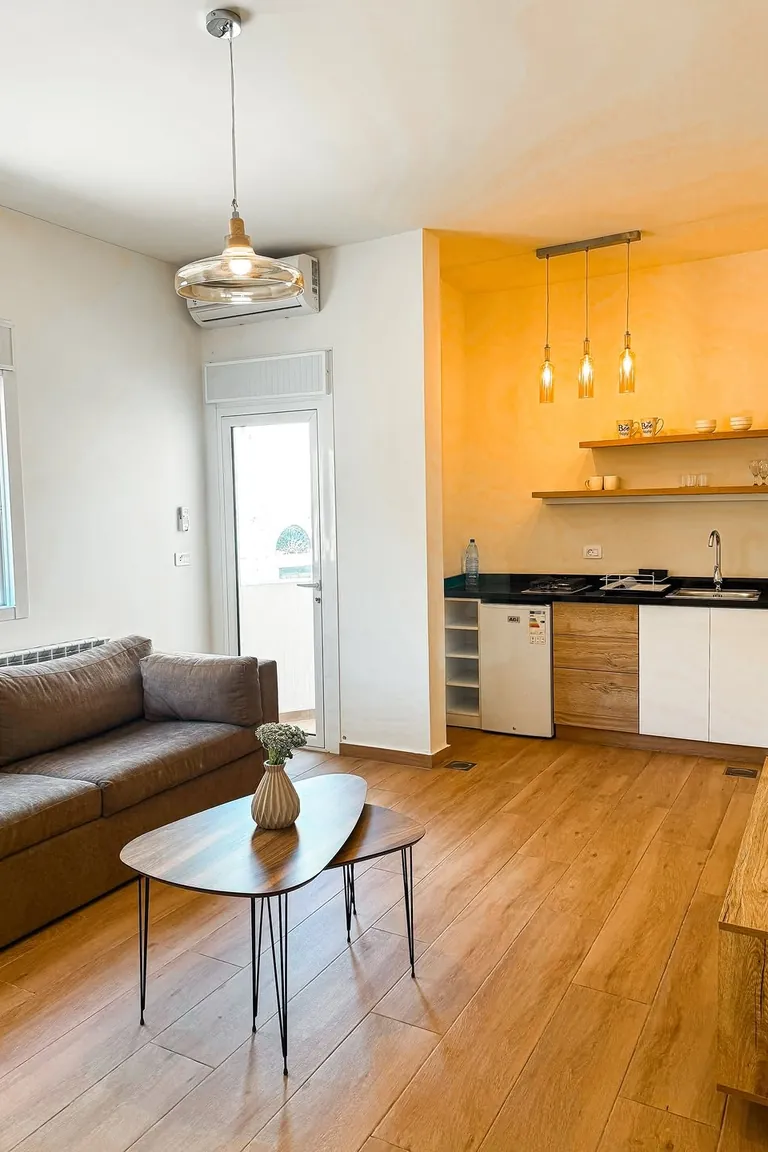 11 Micro Studio Apartment Ideas for Extremely Small Urban Spaces 9 Bright micro studio with a one-wall kitchenette with white cabinets, fridge, hob, and sink, a brown sofa, and wood floors