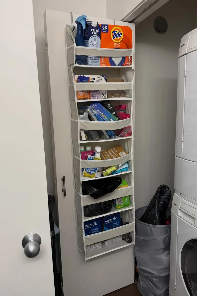 Fabric over the door organizer with clear pockets of small supplies on a laundry closet door