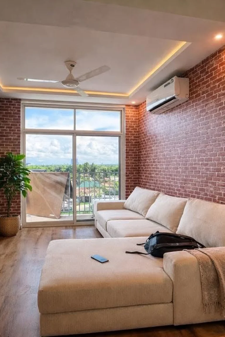 25 Stunning Accent Wall Ideas for Every Room and Style 12 A loft-style living room with a red brick accent wall behind a cream sectional sofa, a floor lamp, wood flooring, a television wall, and large windows opening to a balcony