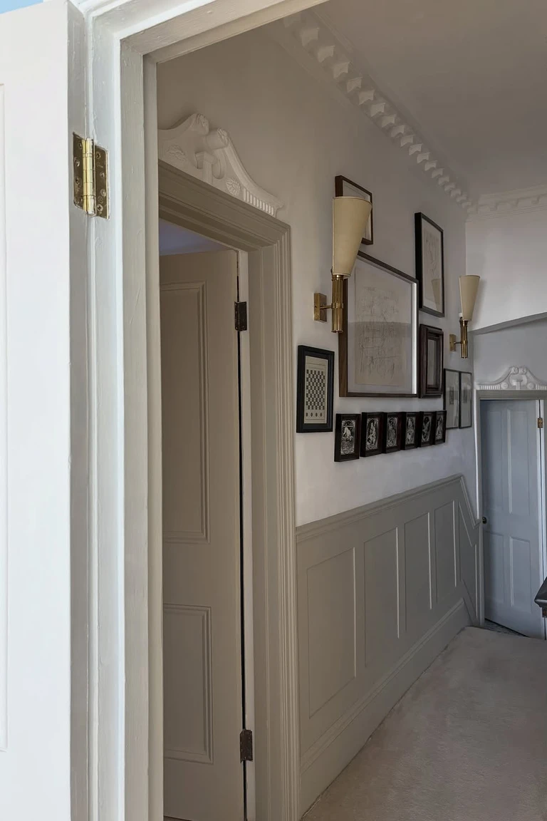Hallway with greige paneled wainscoting, brass wall sconces and framed art