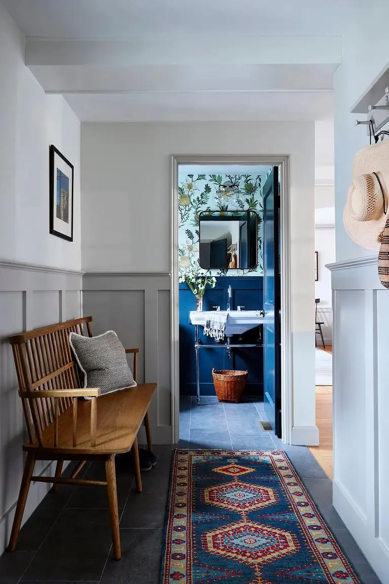 Colonial entry hallway with gray wainscoting, a wooden bench, and a patterned runner