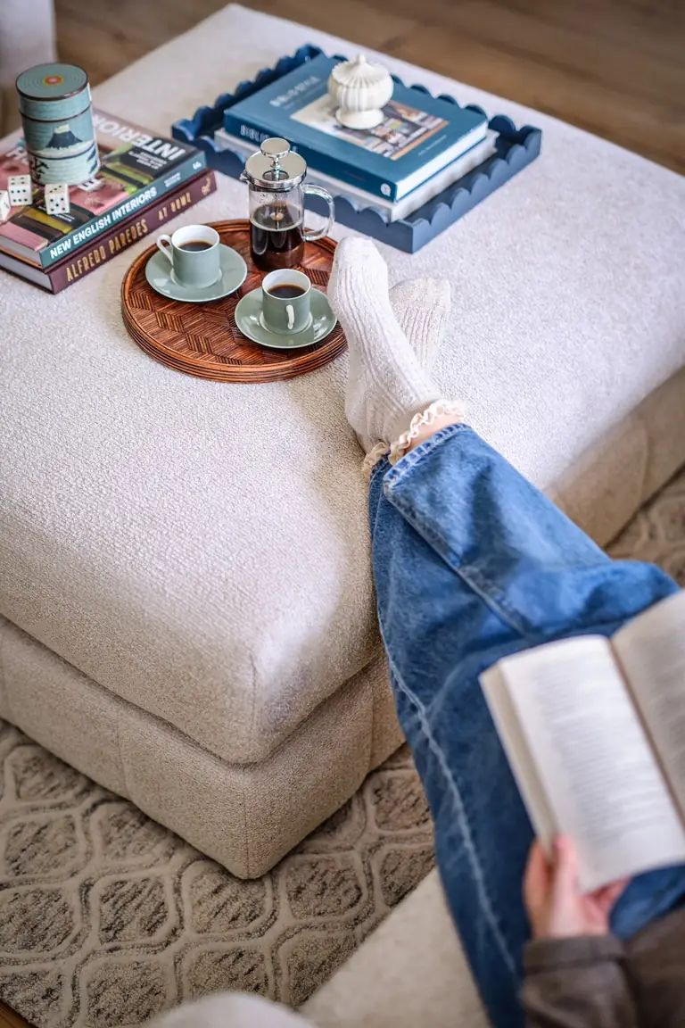Feet up on a large ottoman with a tray of coffee in a cozy corner, an open book in hand
