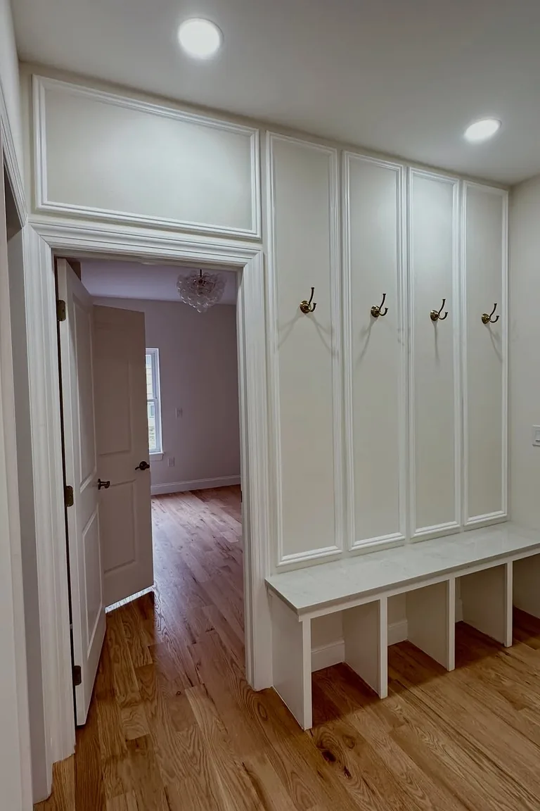 Entryway with white panel molding, brass wall hooks, and a built in bench with cubbies