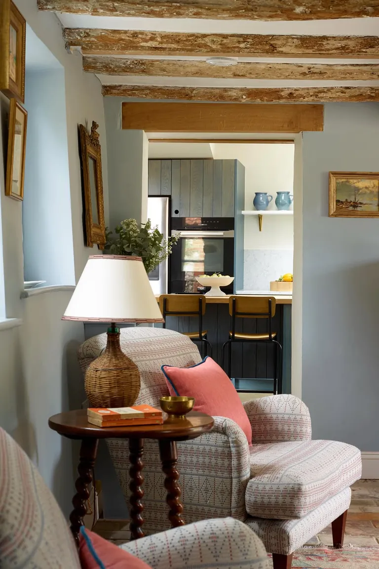 18 Small Kitchen Partition Ideas 15 Living room armchairs looking through a wide cased opening into a blue kitchen with a counter and stools