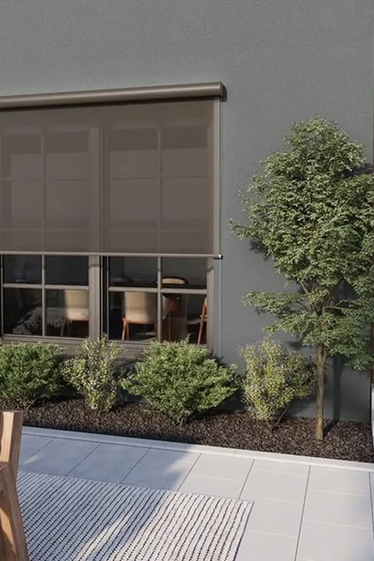House window covered by a lowered brown mesh exterior shade screen, patio sofa corner and shrubs in front