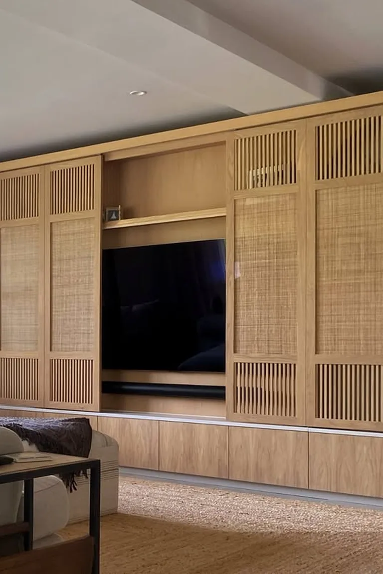 A full media wall with light wood sliding cane panels partly covering a wall mounted television, with open shelving and a sofa in front.