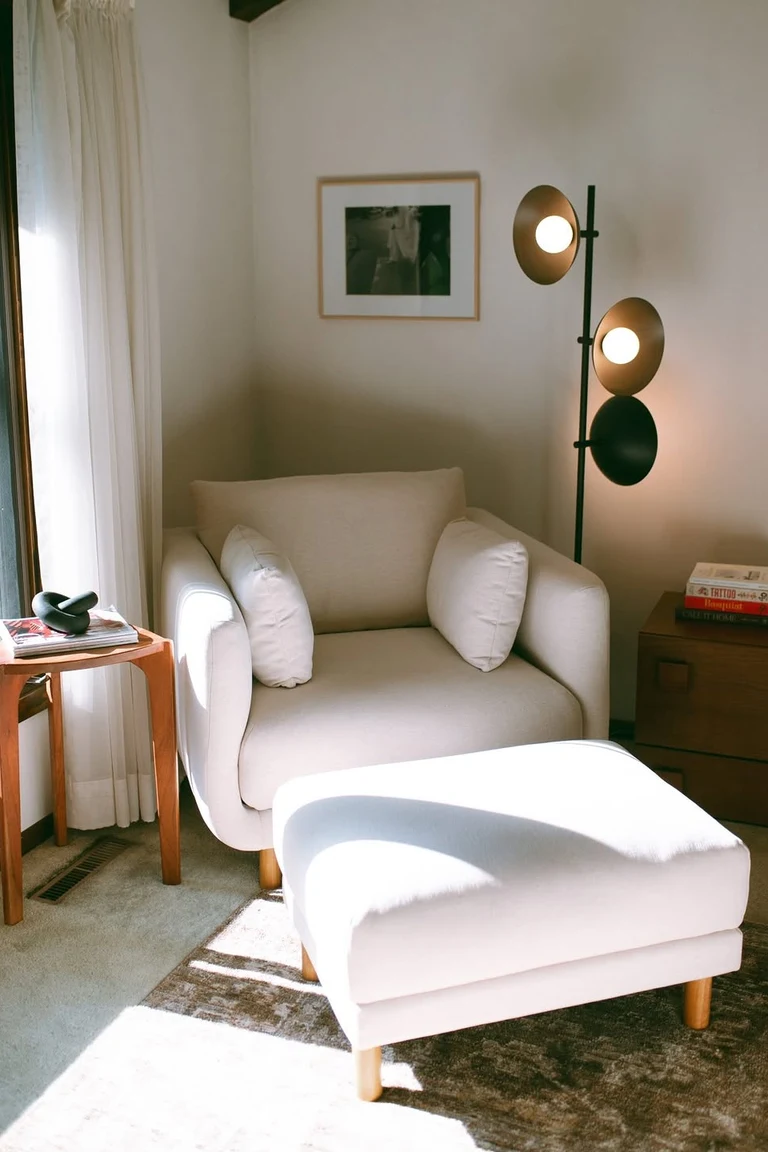 20 Renter-Friendly Bedroom Ideas for a Cozy Space Without Painting 16 Reading corner with a cream armchair, an ottoman, and a floor lamp beside a sunny bedroom window