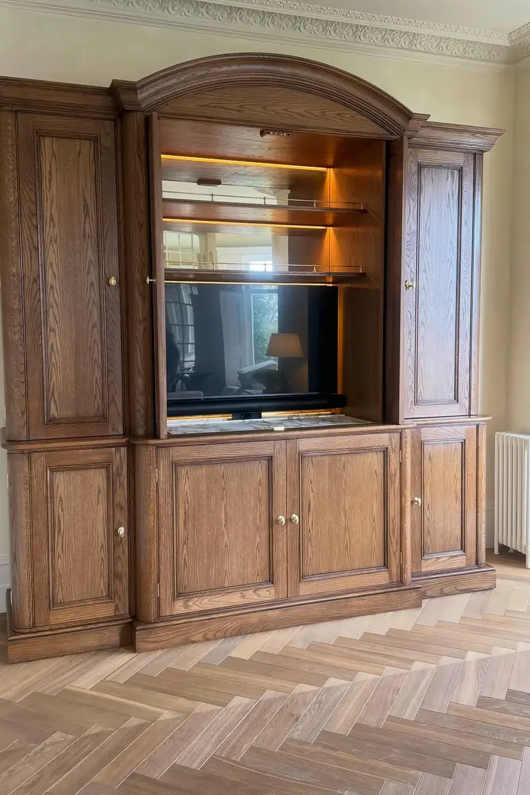 A large arched top oak cabinet with its doors open revealing a television inside, above drawers in a living room.