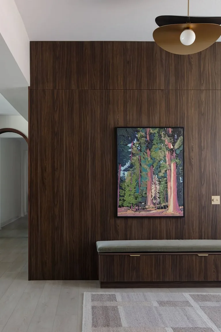 Entryway with floor to ceiling dark walnut wood paneling, a bench, and artwork