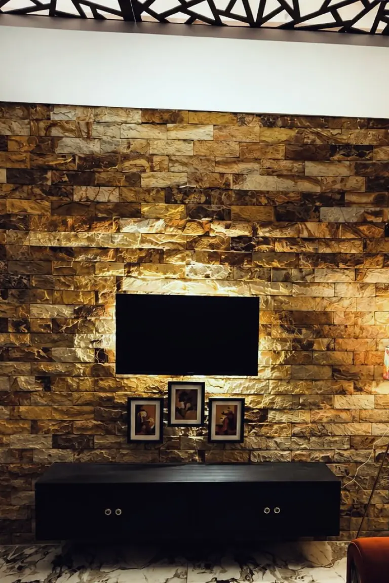 A television mounted on a stacked stone feature wall above a black floating console, with a floor lamp and sofa edge beside it.