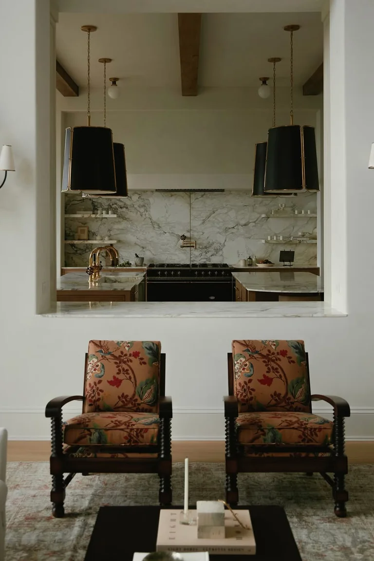 18 Small Kitchen Partition Ideas 19 Living room armchairs facing a wide pass-through window with a marble shelf into a kitchen with a range