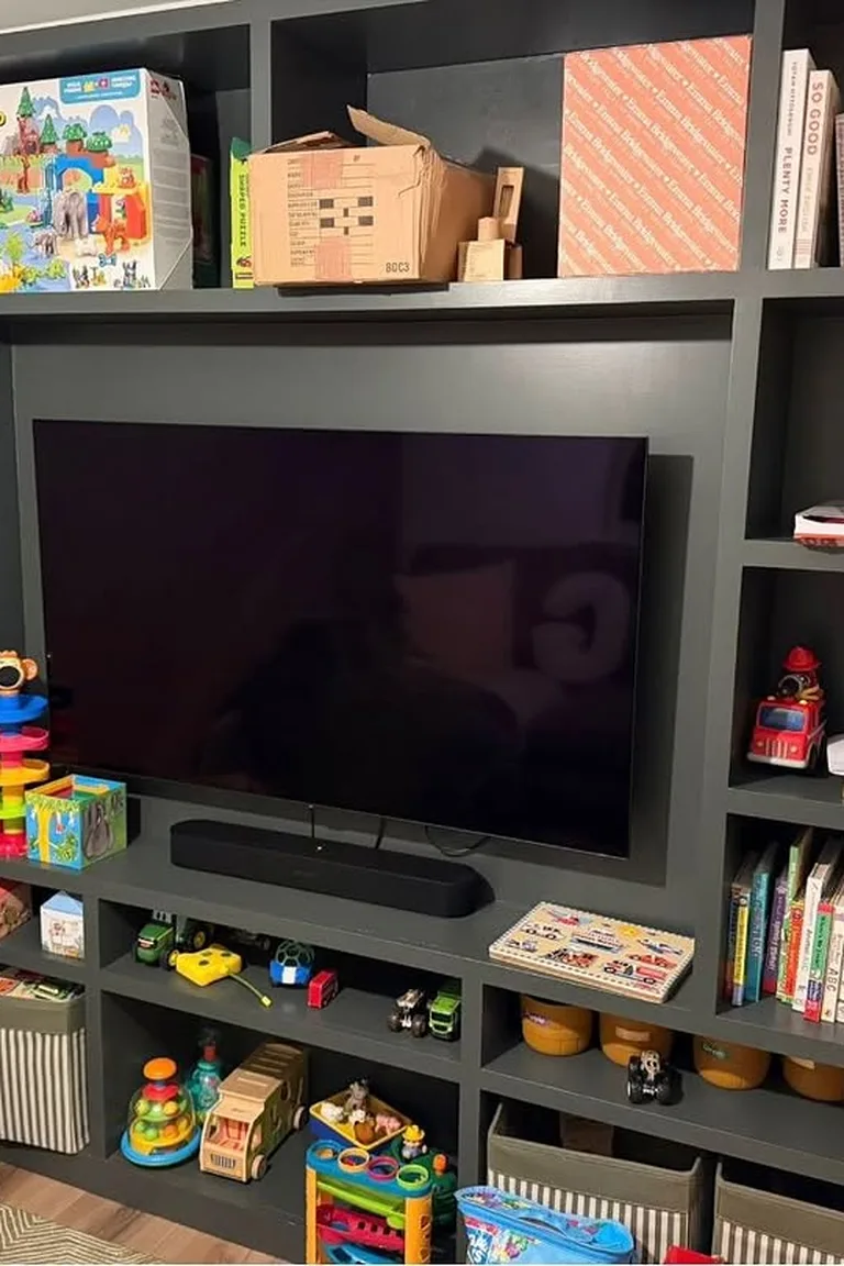 A dark built in family room media wall with a television surrounded by open shelves holding toy boxes, books, and storage baskets.