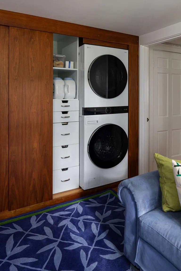 Built in laundry closet with stacked machines, shelving, and drawers in the side gap