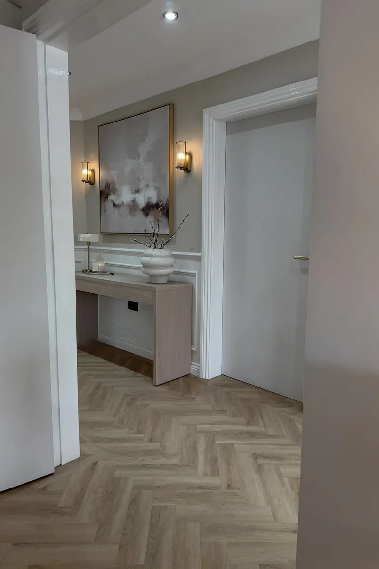Small entryway with white wainscoting, brass wall lights, and a light wood console