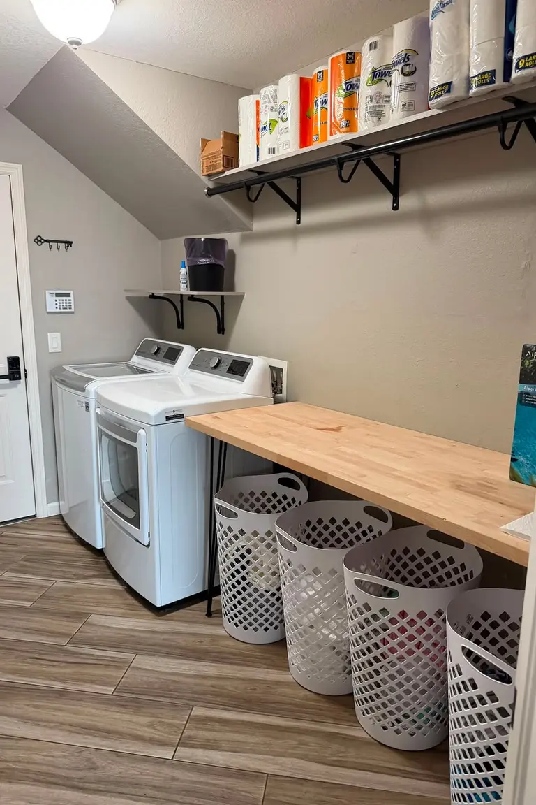 Freshly reset small laundry room with clear surfaces, baskets in place, and an empty folding surface