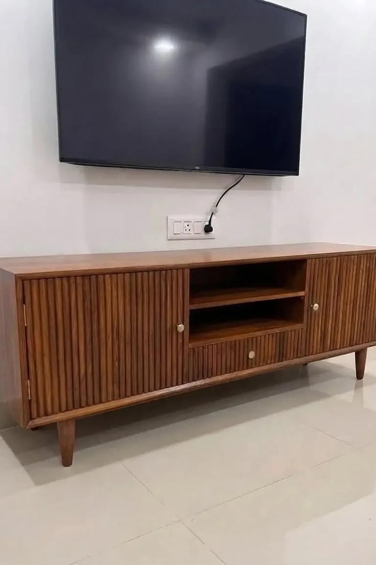 A mid century modern teak TV unit with fluted doors and tapered legs beneath a wall mounted television.