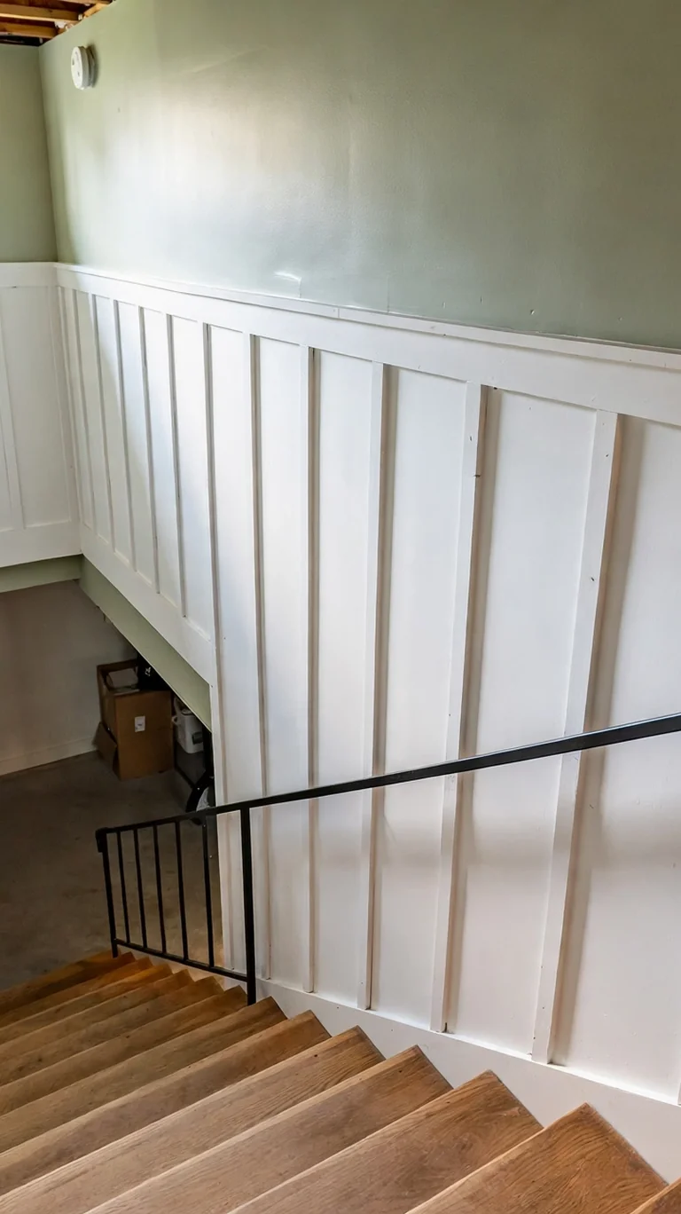 Stairwell wall with white board and batten paneling alongside basement stairs.